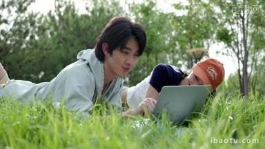 青年情侣趴在草地上用电脑